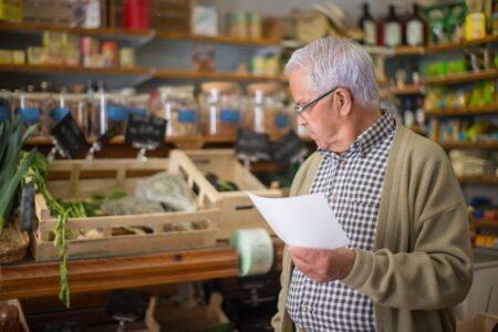 Man reading his shopping list in a grocery store aisle while comparing prices
