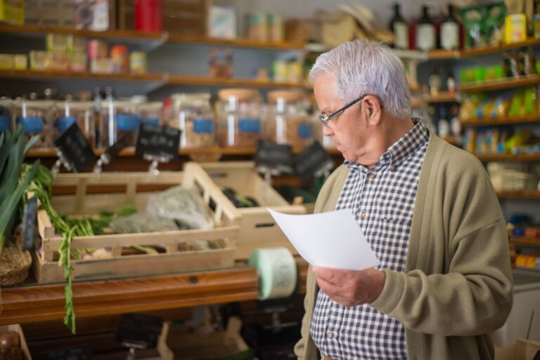 Man reading his shopping list in a grocery store aisle while comparing prices